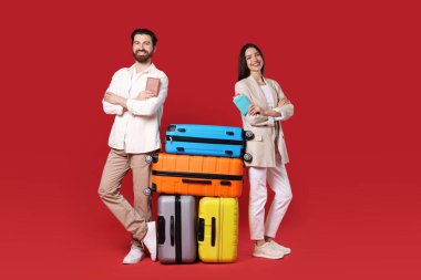 Kırmızı arka planda bavulları, pasaportları ve biletleri olan mutlu çift.