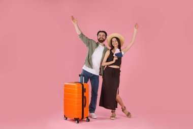 Bavulu, pasaportu ve pembe arka planda biletleri olan mutlu çift.