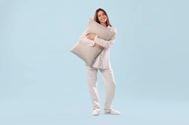 Açık mavi arka planda yastıklı şık pijamalı güzel bir kadın.