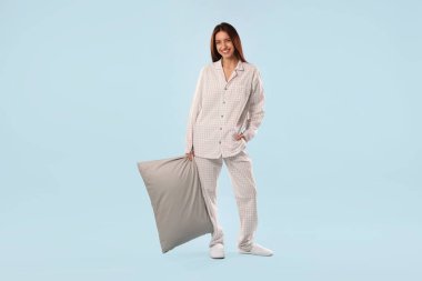 Açık mavi arka planda yastıklı şık pijamalı güzel bir kadın.