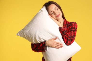 Sarı arka planda yastıklı şık pijamalı bir kadın.