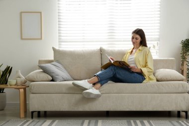 Dergisi olan kadın evinde kanepenin yanında dinleniyor, mesaj için yer var.