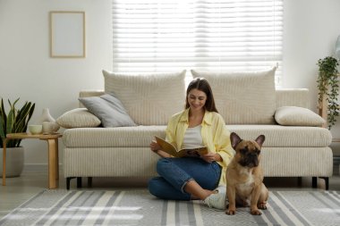 Şirin köpeği ve dergisiyle evdeki kanepenin yanında dinlenen bir kadın.