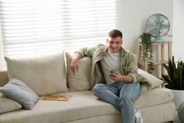 Akıllı telefonlu genç adam evdeki kanepede dinleniyor, mesaj atmak için yer var.