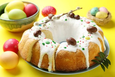 Lezzetli Paskalya pastası, boyanmış yumurtalar, söğüt dalı ve sarı arka planda yeşil yapraklar, yakın plan.