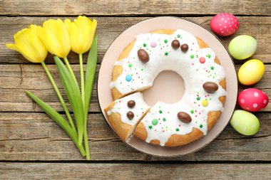 Lezzetli Paskalya pastası, boyanmış yumurtalar ve ahşap masada sarı laleler.