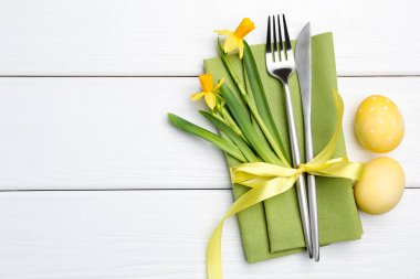 Paskalya sofrası. Nergisli güzel gümüş takımlar ve beyaz ahşap arka planda boyanmış yumurtalar, üst manzara. Metin için boşluk