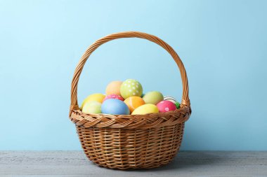 Hasır sepetin içine boyanmış Paskalya yumurtaları açık mavi arka plana karşı gri ahşap masa üzerinde