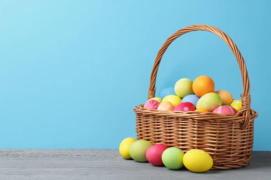 Hasır sepetin içine boyanmış Paskalya yumurtaları açık mavi arka planda gri ahşap masa üzerinde. Metin için boşluk