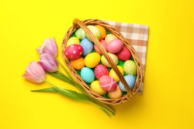 Sarı arka planda boyanmış yumurtalar ve laleler olan Paskalya sepeti düz yatıyordu.