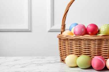 Hasır sepete boyanmış Paskalya yumurtaları beyaz duvarın yanındaki beyaz mermer masada, yakın plan. Metin için boşluk