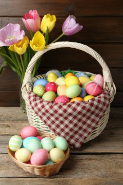 Hasır sepete boyanmış Paskalya yumurtaları ve ahşap masada güzel laleler.