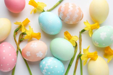 Beyaz arka planda boyanmış Paskalya yumurtaları ve güzel nergisler.