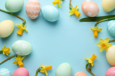 Boyanmış Paskalya yumurtaları ve açık mavi arka planda güzel nergisler. Metin için boşluk