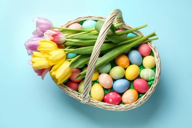 Açık mavi zemin üzerinde boyanmış yumurta ve laleler olan Paskalya sepeti, üst manzara.