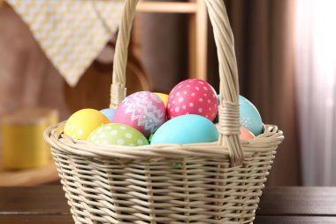 Kapalı alandaki ahşap masada boyanmış yumurtaların olduğu Paskalya sepeti, yakın plan.