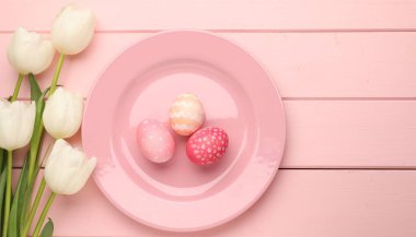 Paskalya kutlaması. Çiçeklerle süslü bir ortam ve pembe ahşap masaya boyanmış yumurtalar. Metin için boşluk