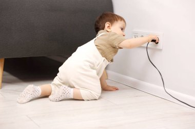 Evde çocuk güvenliği. Küçük çocuk içerideki elektrik prizinin fişini çekiyor.