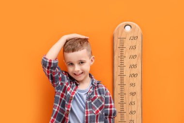 Küçük çocuk turuncu duvarın yanında boyunu ölçüyor.