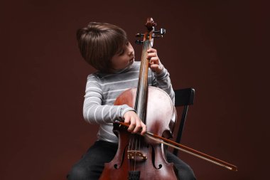 Kahverengi arka planda keman çalan sevimli küçük çocuk.