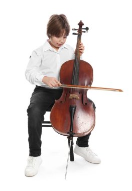 Küçük çocuk beyaz arka planda sandalyede keman çalıyor.