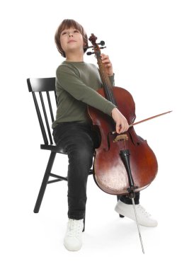 Küçük çocuk beyaz arka planda sandalyede keman çalıyor.