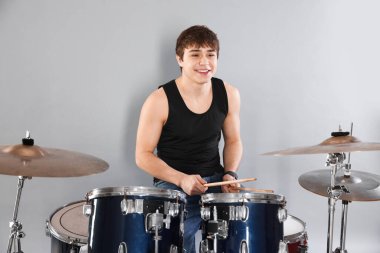 Gri arka planda davul çalmayı öğrenen güler yüzlü genç çocuk.