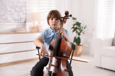 Evdeki sandalyede keman çalan küçük çocuk.