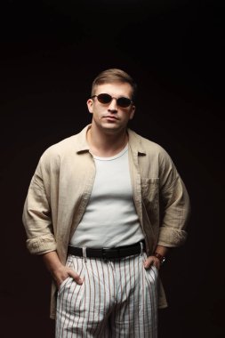 Moda modeli. Siyah arka planda poz veren güneş gözlüklü yakışıklı bir adam.