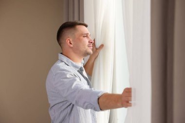 Evdeki bej duvarın yanında güzel perdeler açan adam.