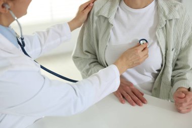 Steteskoplu bir kardiyolog klinikteki beyaz masada kalp atışlarını dinliyor.