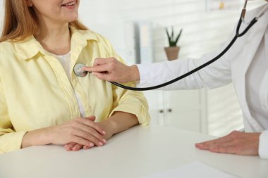 Steteskoplu bir kardiyolog klinikteki beyaz masada kalp atışlarını dinliyor.