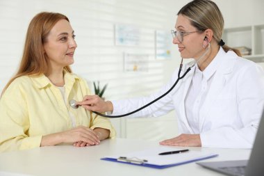 Steteskopla gülümseyen kardiyolog klinikteki hastanın kalp atışlarını dinliyor.