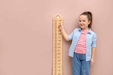 Bej duvarın yanında boyunu grafikle ölçen küçük bir kız. Metin için boşluk