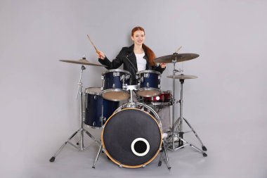 Açık gri arka planda bagetleri ve davulları olan genç bir kız.