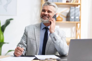 Ofiste akıllı telefonla konuşan takım elbiseli güler yüzlü bir işadamı.