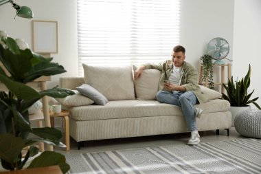 Akıllı telefonlu genç adam evdeki kanepede dinleniyor.