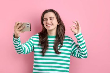 Mutlu kadın pembe arka planda selfie çekerken iyi niyet gösteriyor.