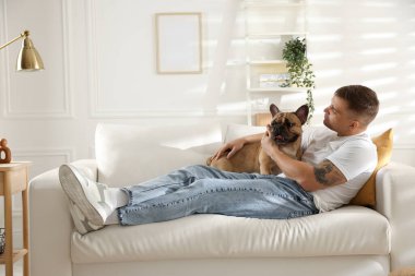 Evdeki kanepede dinlenen sevimli köpeğiyle genç bir adam.