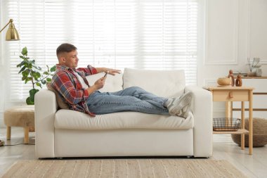 Akıllı telefonlu genç adam evdeki kanepede dinleniyor.