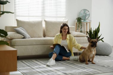 Şirin köpeği ve dergisiyle evdeki kanepenin yanında dinlenen bir kadın.