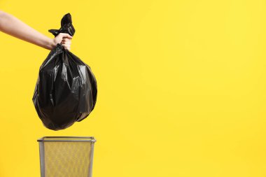 Sarı arka planda çöp poşeti ve çöp tenekesi olan bir kadın, yakın plan. Metin için boşluk