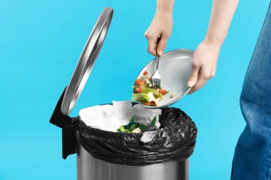 Açık mavi arka planda çöp tenekesine yemek atan kadın, yakın plan.