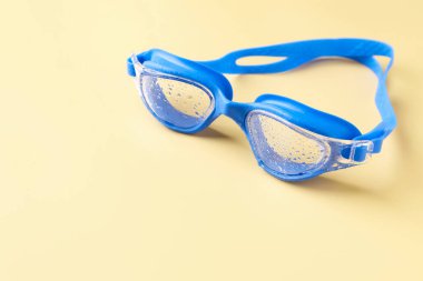 Sarı arka planda su damlaları olan yüzme gözlükleri, yakın plan. Metin için boşluk