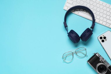 Kulaklıklar, akıllı telefon, bilgisayar klavyesi, klasik kamera ve açık mavi arka planda gözlük, düz konum. Metin için boşluk