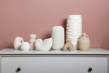 Koyu bej duvarın yanındaki dolapta farklı güzel vazolar var.