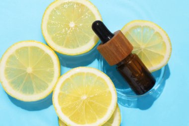 Bir şişe kozmetik ürünü ve limon dilimleri açık mavi arka planda, düz yerde.