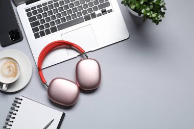 Kulaklıklar, akıllı telefon, dizüstü bilgisayar, kahve, kırtasiye malzemeleri ve açık gri arka planda çiçek dekoru, düz yatak. Metin için boşluk