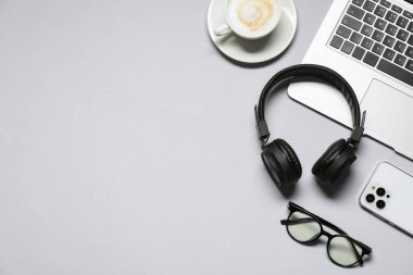 Kulaklıklar, dizüstü bilgisayarlar, kahve, akıllı telefon ve açık gri arka planda gözlükler, düz konum. Metin için boşluk