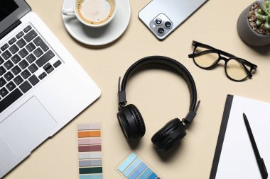 Kulaklıklar, dizüstü bilgisayarlar, akıllı telefonlar, gözlükler, kahve, çiçek dekoru ve bej arka planda kırtasiye malzemesi.